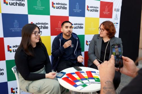 Francisca Contreras, Nicolás Fuentes y Leslie Jiménez sentados conversando, con fondo Admision UCHILE y frente un celular transmitiendo el live del diálogo