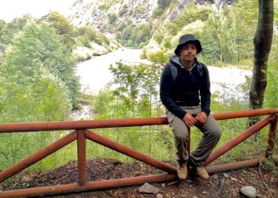 Francisco Quinán, posando en el exterior, sentado en una baranda, con un río y mucha vegetación de fondo