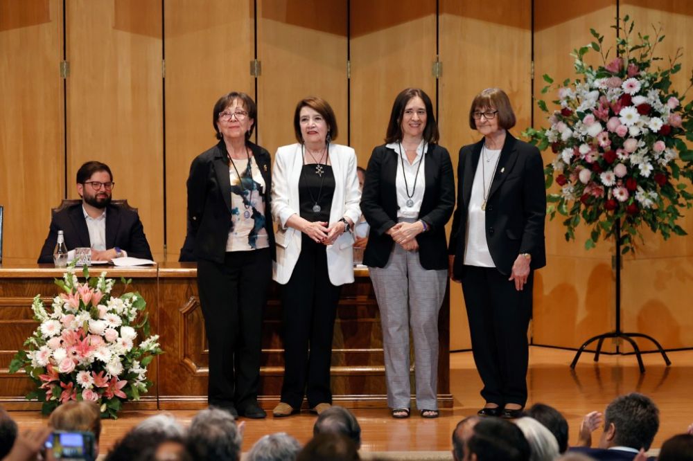 en la imagen podemos ver el escenario con las tres consejeras galardonadas paradas junto a la rectora Rosa Devés. De fondo, se puede ver al Presidente de la República, Gabriel Boric. 