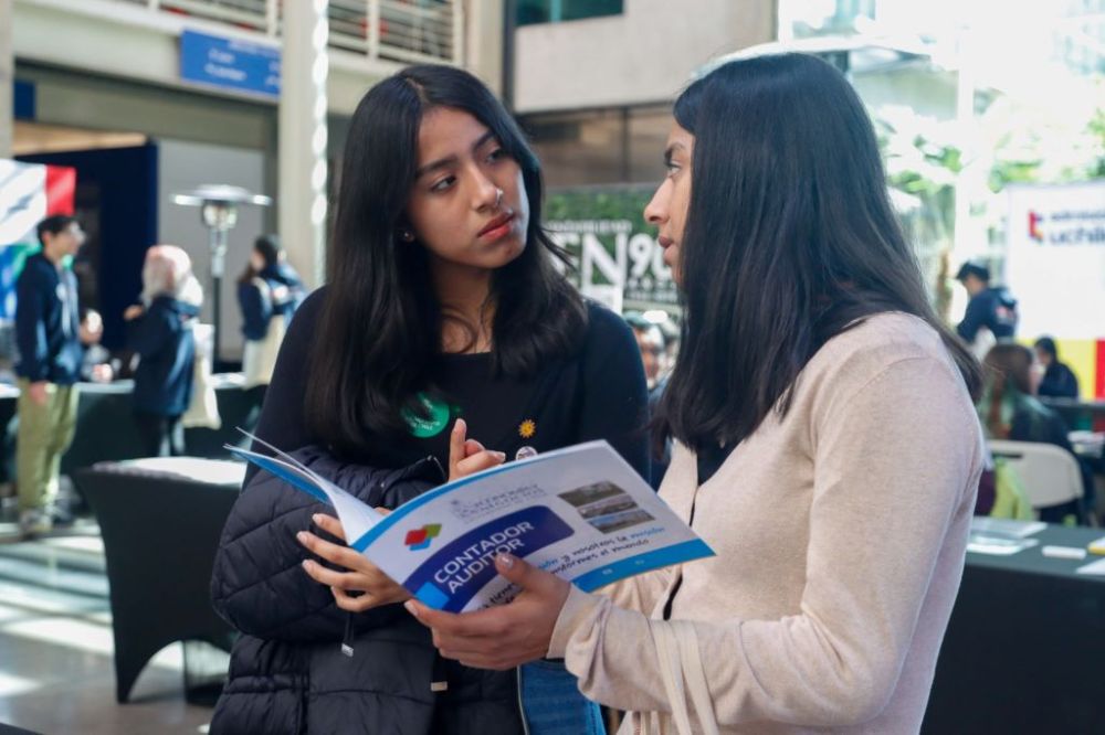 Dos postulantes, mirándose frente a frente, mientras sostienen material de difusión de la carrera de Contador Auditor de la U. de Chile