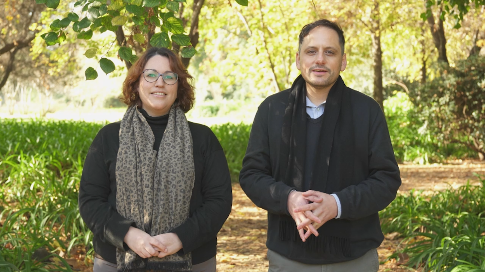 Docentes de la U. de Chile Leslie Jiménez y Sergio Celis mirando a la cámara, con fondo exterior de arbustos y árboles