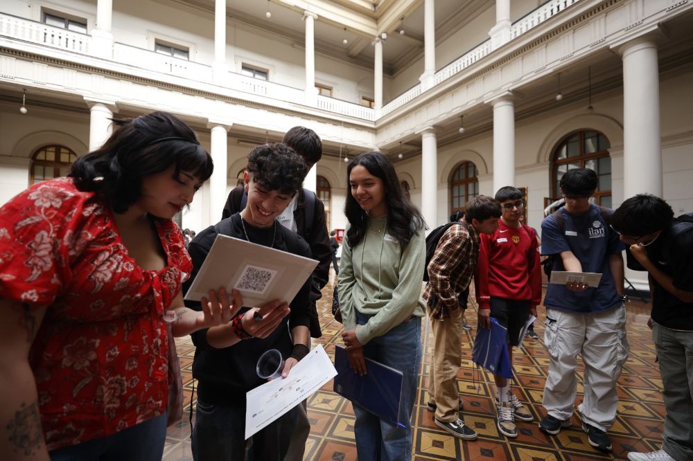 Entudiantes en grupo, mirando una lámina, en el patio Andrés Bello de Casa Central