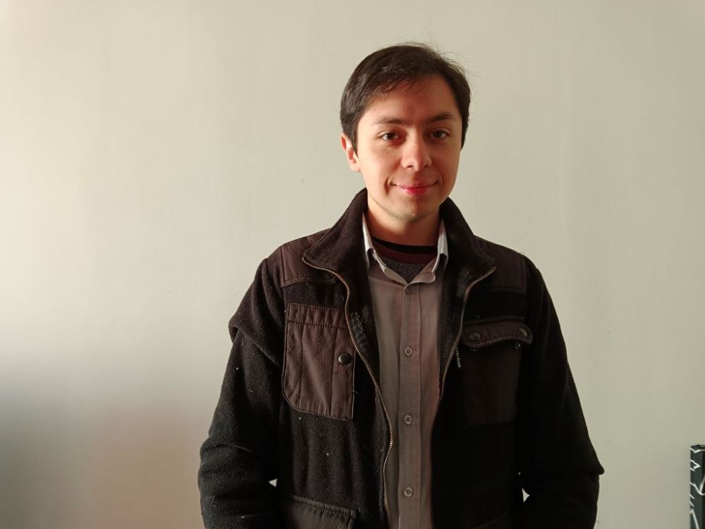 Medio plano de Juan Pablo Cruz, quien sonríe a la cámara. Fondo blanco. 