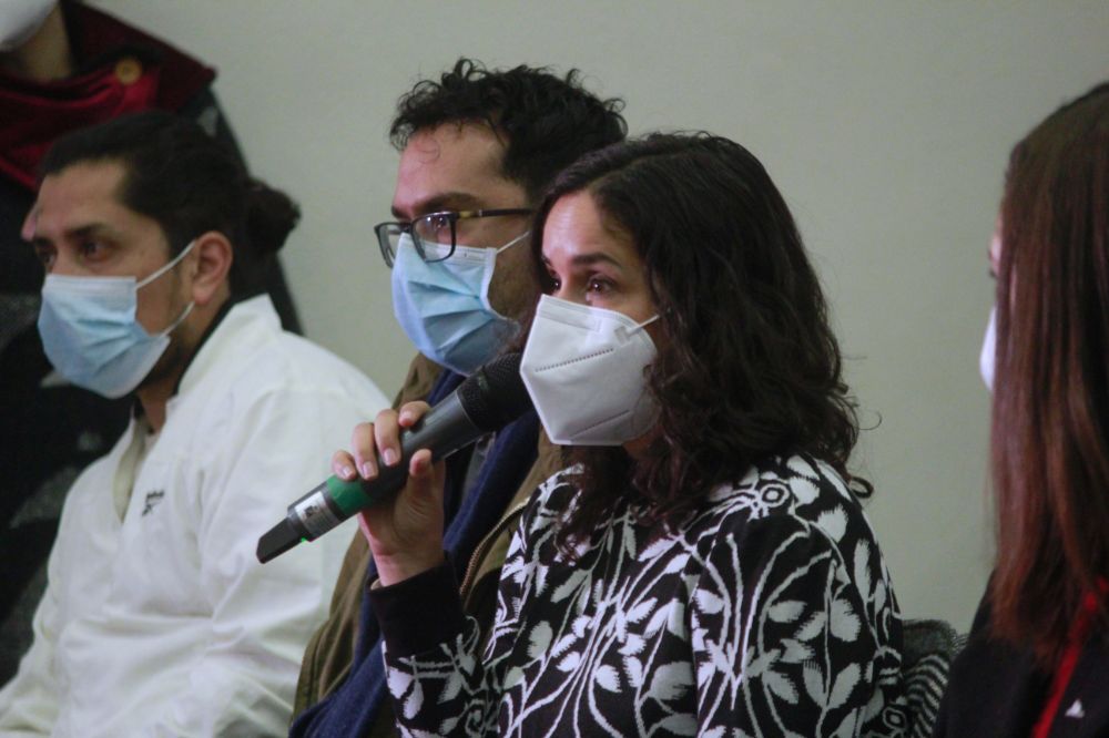 Académica con micrófono y mascarilla, haciendo una pregunta.