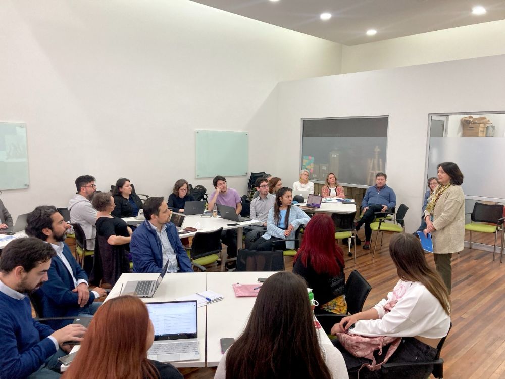 Leonor Armanet, frente a grupos de académicas/os, funcionarias/os y estudiantes sentados en mesas de trabajo.