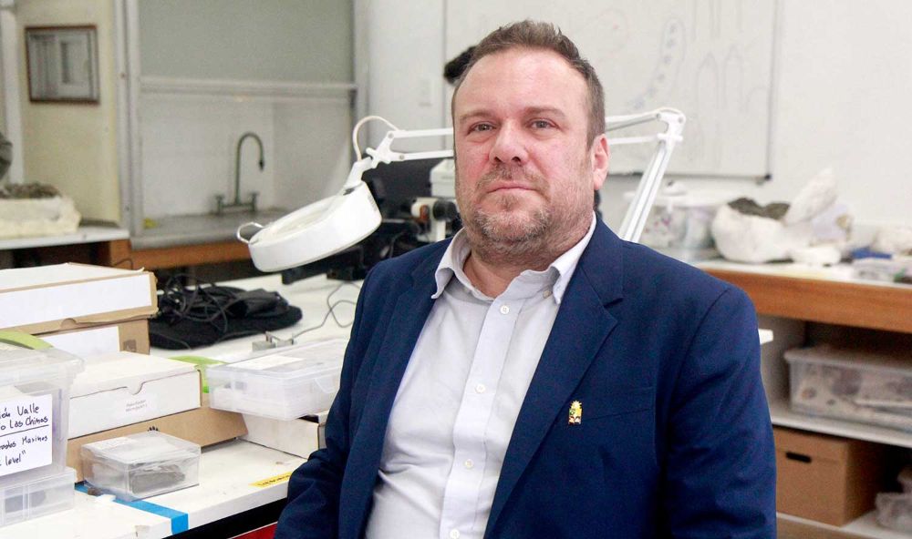 Alexander Vargas vistiendo un vestón azul, sentado en su laboratorio