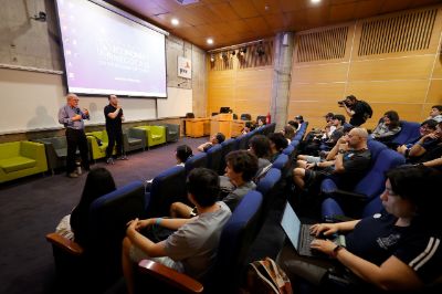 Auditorio con estudiantes y José Maza adelante, conversando con ellas y ellos