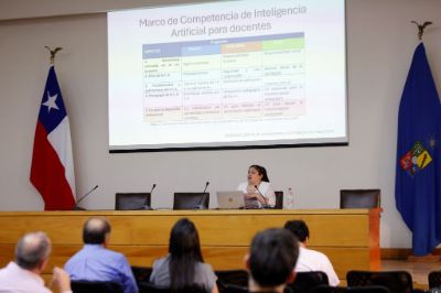 Público desde atrás, se ve la pantalla donde dice "Marco de competencia de Inteligencia Artificial para docentes" y la profesora Beatriz Bustamante exponiendo