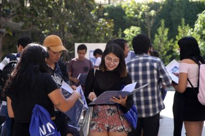 Estudiantes en un patio, donde destaca una estudiante sonriendo y mirando una carpeta, en el contexto de inducción a la vida universitaria