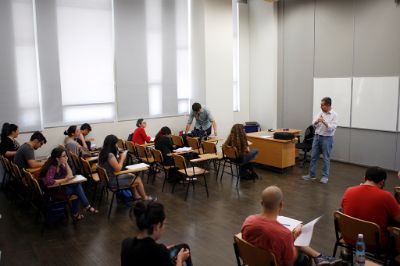 Sala de clases con estudiantes sentadas y sentados, y un profesor parado al frente