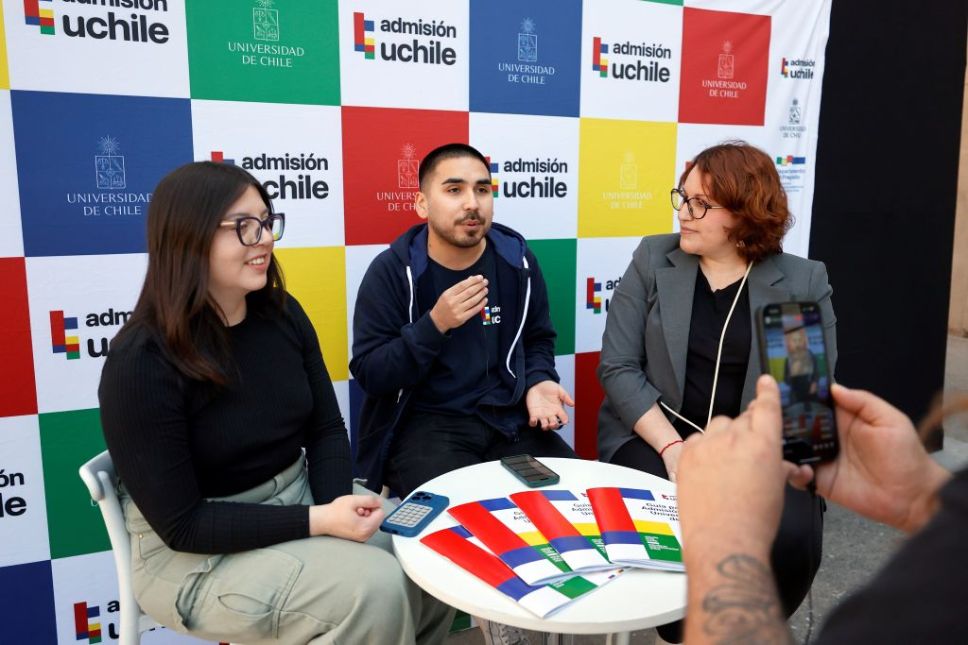 Francisca Contreras, Nicolás Fuentes y Leslie Jiménez sentados conversando, con fondo Admision UCHILE y frente un celular transmitiendo el live del diálogo