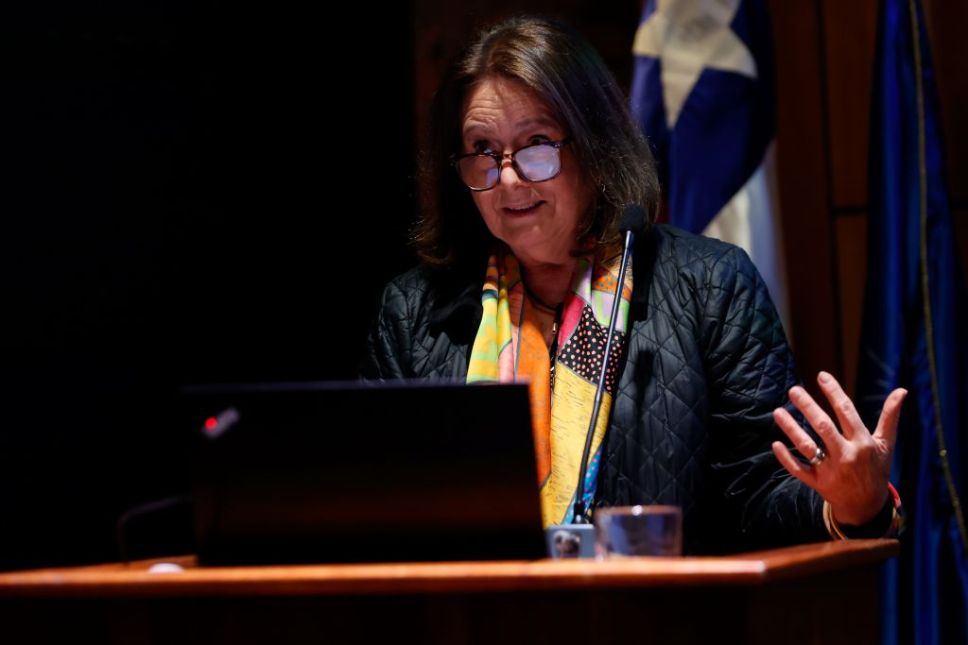 Medio plano de Leonor Armanet, hablando y gesticulando con las manos en la testera del auditorio de la FAU de la U. de Chile
