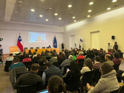 Desde atrás se ve la sala Eloísa Díaz llena de gente. Adelante, en pantalla gigante, Francesc Pedró en videollamada desde España.