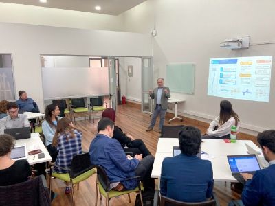 Sala, con ppt proyectado, profesor Luis Osandón al frente y distintos miembros de la comunidad universitaria escuchando desde mesas de trabajo.