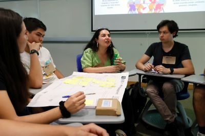 La foto muestra a una estudiante hablando frente a sus compañeras/os de la mesa de trabajo. 